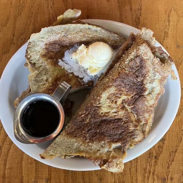 Golden brown French toast with melting butter and a side of syrup on a white plate.