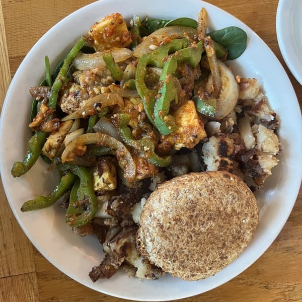 A vegetarian scramble with tofu, green peppers, onions, and home fries, served with a side of toast.