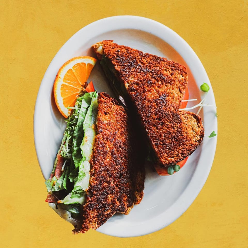 A vegetarian sandwich with toasted bread, lettuce, and tomato, served with an orange slice.