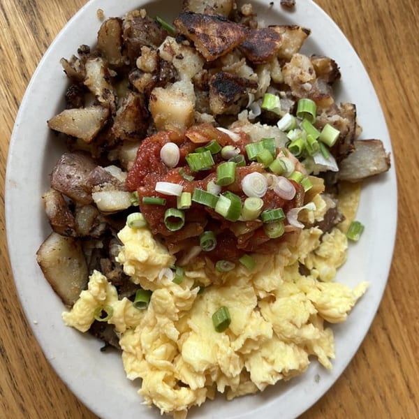 A vegetarian breakfast plate with scrambled eggs, home fries, salsa, and green onions.