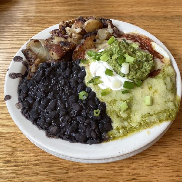 Vegetarian breakfast plate with black beans, roasted potatoes, green sauce, guacamole, and sour cream.