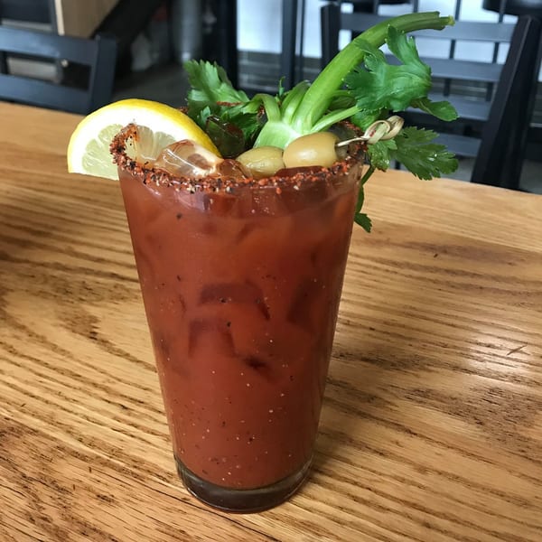 A Bloody Mary cocktail with a lemon slice, olives, and celery on a wooden table.