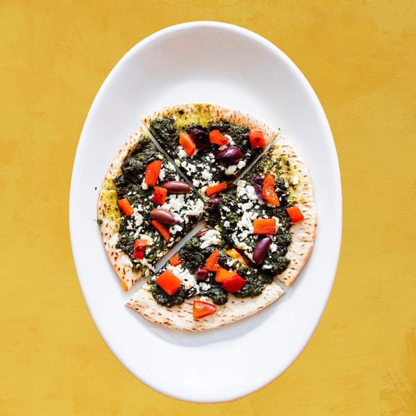 Sunlight Cafe's vegetarian flatbread with pesto, feta, red peppers, and olives on a white plate.